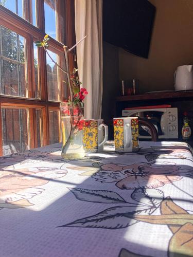 a table with a table cloth with flowers and mugs on it at Mini cabaña El Solcito, tranquilidad a dos cuadras de la Laguna de Chascomús in Chascomús