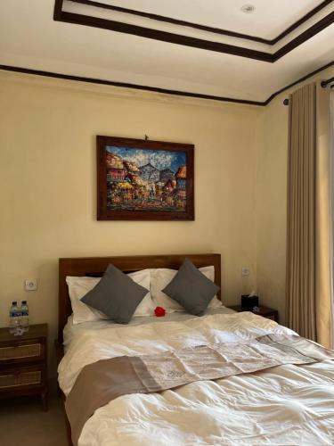a bedroom with a white bed with a painting on the wall at Oemah Dharma Garden View by EPS in Gianyar