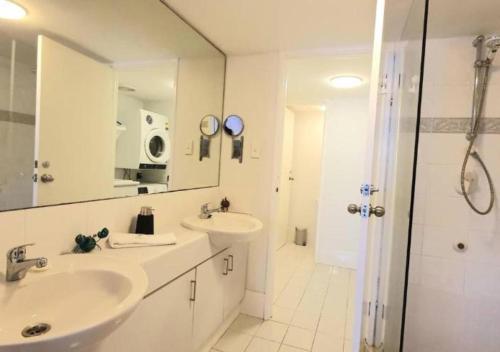 a white bathroom with two sinks and a shower at Sandcastles Beachfront Luxury Retreat Apartment in Perth