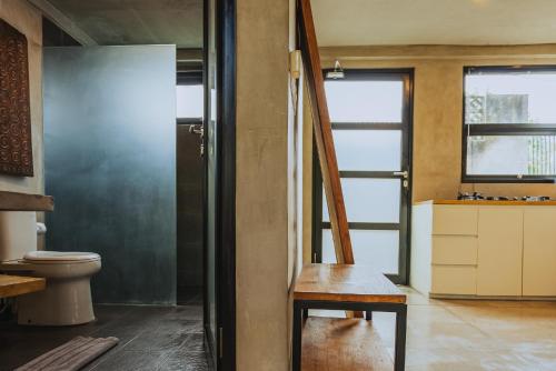 a bathroom with a toilet and a wooden chair at Berawa Loft by Betterplace in Canggu
