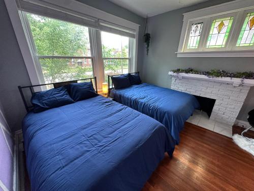 two beds in a bedroom with blue sheets and a fireplace at Cute Neighborhood Rainbow Apt in Saint Louis