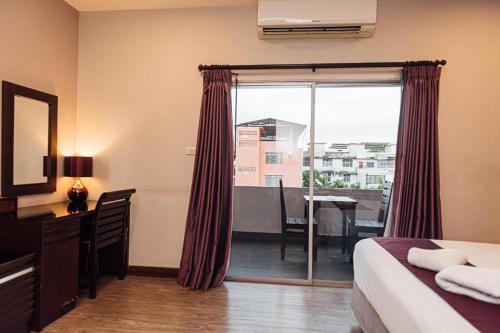a hotel room with a bed and a desk and a window at Gazebo Resort Pattaya in Pattaya Central