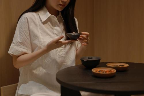 a woman in a white shirt holding a bowl next to a table at Aank Ryokan Hotel Ansan Seonbu Branch in Ansan