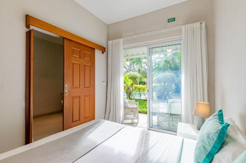 1 dormitorio con 1 cama y puerta a un balcón en Kisana Residence - Pleasant apartment with pool, close to beach, en Pointe aux Cannoniers