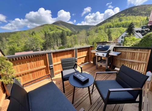 a deck with chairs and a grill with mountains in the background at Chata u lanovky Pustevny in Trojanovice