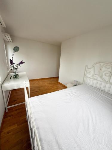 a white bedroom with a bed and a table with a lamp at Room in Homestay with amazing view of lake - Zimmer in einer Gastfamilie mit herrlichem Blick auf den See in Feusisberg