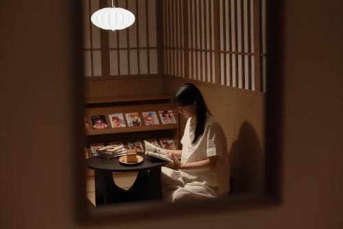 a woman sitting at a table reading a book at Aank Ryokan Hotel Ansan Seonbu Branch in Ansan