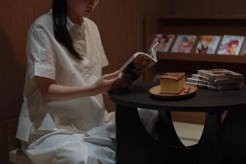 a woman reading a book next to a table with a piece of cake at Aank Ryokan Hotel Ansan Seonbu Branch in Ansan