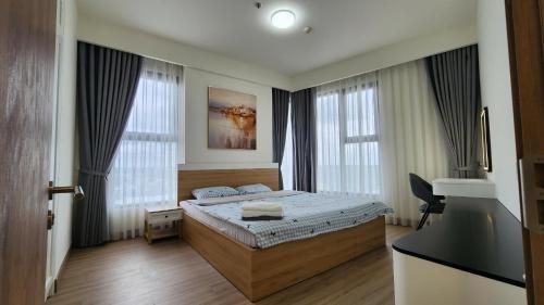 a bedroom with a bed and a desk and two windows at Homie's The Glory Apartment in Thu Dau Mot