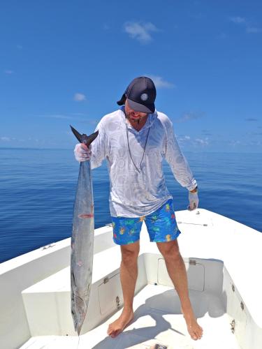 a man standing on a boat holding a fish at Blue Wave Hotel Maldives in Kudahuvadhoo