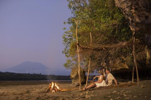 two people sitting next to a fire on the beach at Pramana Nusa Ceningan in Nusa Lembongan