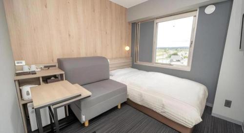 a bedroom with a bed and a chair and a window at Super Hotel Arai-Niigata in Myoko