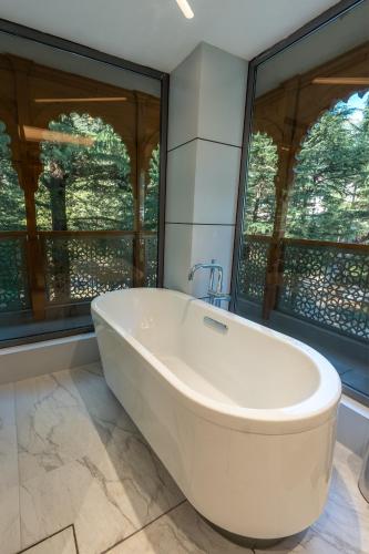 a bath tub in a bathroom with large windows at Mastiff Select Mandavya Dharamkot, McLeodganj in Dharamshala