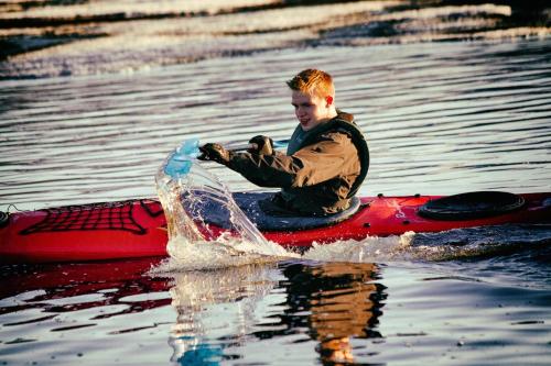 a man riding on top of a red kayak in the water at Tundrea Holiday Resort in Kilpisjärvi