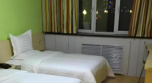 two beds in a hotel room with a window at 7 Days Inn Hami Baofeng Market in Qumul