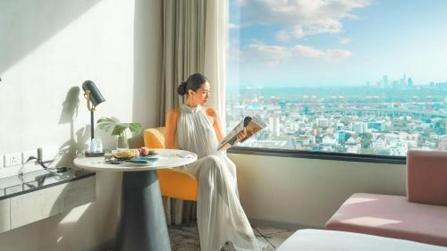 a woman reading a book in a room with a window at Avani Sukhumvit Bangkok Hotel in Bangkok