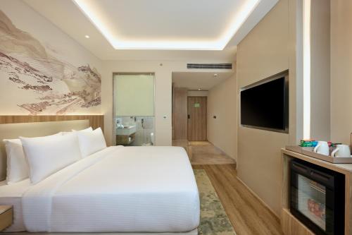 a bedroom with a large white bed and a television at Riviera Sarovar Portico Pathankot in Pathānkot