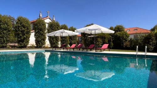 a large swimming pool with two umbrellas and chairs at Feel Discovery Casa Da Capela Douro Valley in Armamar