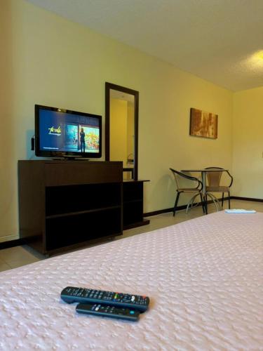 a bedroom with a television and two remote controls on a bed at Studio pé na areia, vista, internet e ar in Macaé