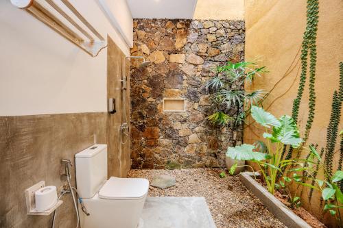 a bathroom with a toilet and a stone wall at Aurora in Unawatuna