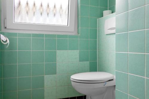 a green tiled bathroom with a toilet and a window at Walnut Tree Apart in Bergisch Gladbach