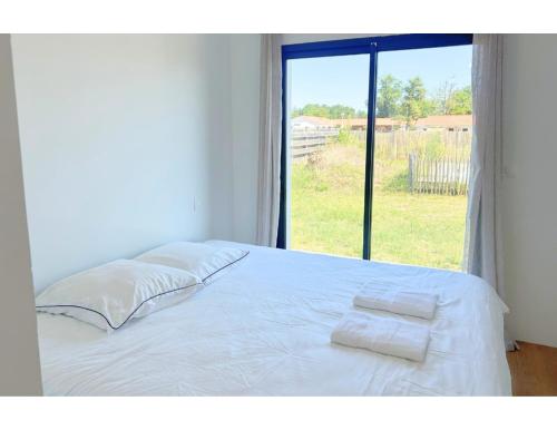 1 cama blanca con 2 almohadas y ventana en Maison Calme Biscarosse avec Piscine - 10 min Plage, en Biscarrosse