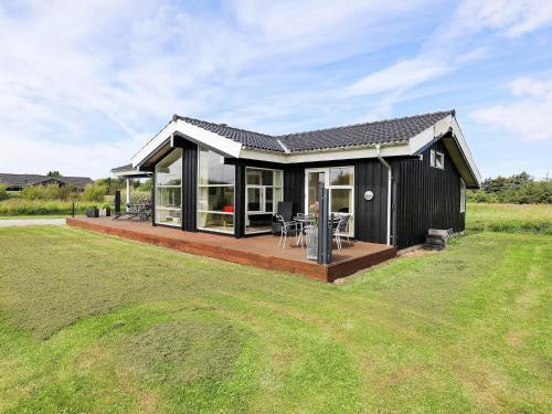 a black house with a deck in a field at 6 person holiday home in Hirtshals in Hirtshals