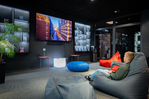 a man sitting on a couch watching a tv at Luna Self Check-in Hotel Klaipeda in Klaipėda