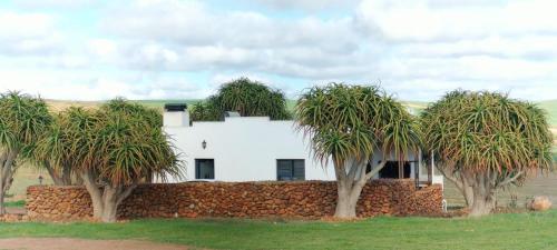 a white house behind a stone wall with trees at Aloe Cottage in Cloeteskraal