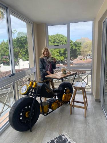 a woman sitting at a table next to a motorcycle at Luxury Holiday Apartment mit 2 Schlafzimmern am Strand von Hout Bay in Hout Bay