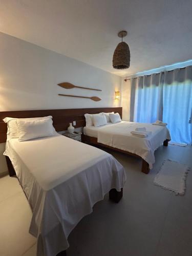 a hotel room with two beds and a window at Kamaiurá Pousada in Caraíva