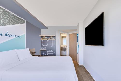a bedroom with a white bed and a flat screen tv at One Ciudad Juarez Alameda Iglesias in Manuel F. Martínez