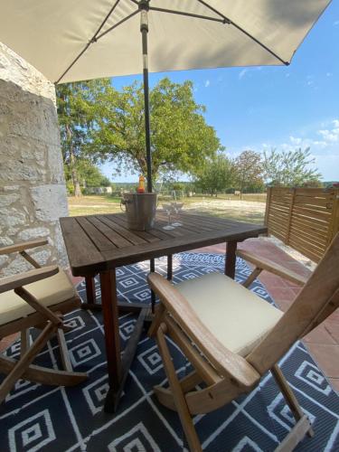 a wooden table and chairs with an umbrella on a patio at Petit Rousset Gite Noyer in Eymet