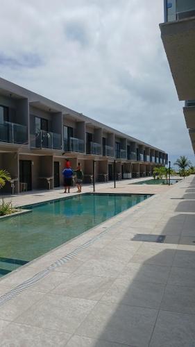 two people standing near a swimming pool in a building at Condomínio Villaggio di Como in Itamaracá