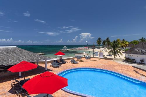 a swimming pool with red umbrellas and the ocean at Grand Muthu Runaway Bay Club Caribbean in Runaway Bay