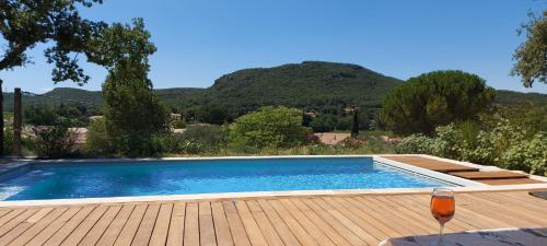 a swimming pool on a wooden deck with a glass of wine at Provence, Uzès, villa climatisée 8 pers avec piscine privée in Gaujac