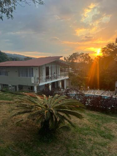 une maison avec un palmier devant un coucher de soleil dans l'établissement Casa Campestre Claro de Luna - Fusagasugá, à Fusagasuga