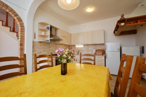 a kitchen with a yellow table with a vase of flowers on it at Kapetanova kuća in Martinšćica
