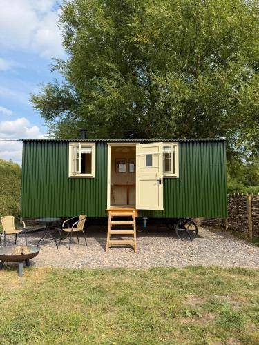 a green tiny house with a ladder and chairs at Cosy Shepherd Hut in Kempsford