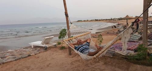 a man laying in a hammock on the beach at Panorama Lodge Nuweiba in Nuweiba