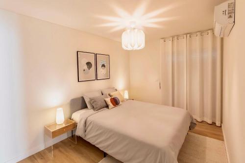 a white bedroom with a bed and a chandelier at MIRA Living in Lisbon