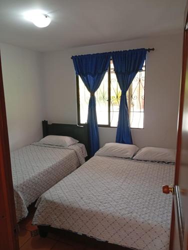 a bedroom with two beds and a window with blue curtains at FINCA Villa luna in Quimbaya