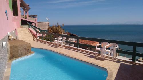 a swimming pool with two chairs and the ocean at Pousada do Sergio in Barra de Guaratiba