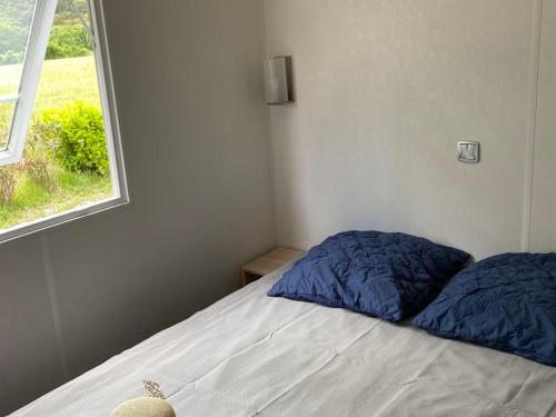 a bed with blue pillows in a bedroom with a window at Mobil home confortable avec terrasse pour 6 personnes - API-1-52-393 in Saint-Maurice-dʼIbie