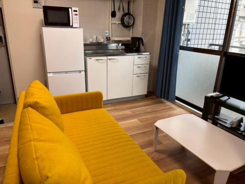 a living room with a yellow couch and a kitchen at お宿あびこシルバーハイツ in Osaka