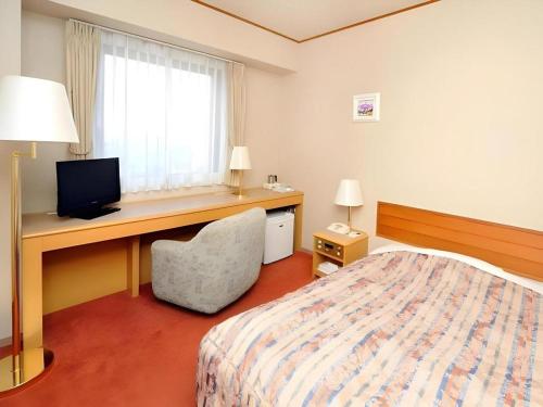 a hotel room with a bed and a desk with a television at Hotel Grand Shinonome in Tsukuba