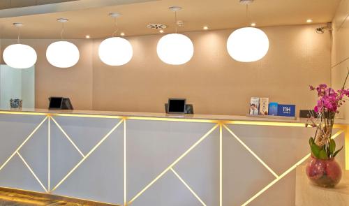 a lobby with a counter with flowers and lights at NH Ciudad de Zaragoza in Zaragoza