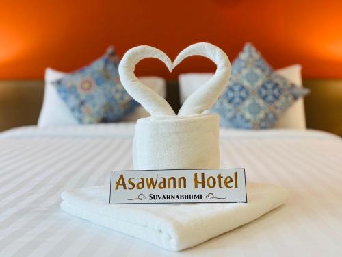 a towel with a swan hotel sign on a bed at Asawann Hotel Suvarnabhumi in Ban Hua Takhe