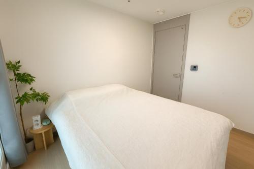 a white bedroom with a bed and a clock on the wall at E 2BR 60m2 Newly Built High Floor APT 2min to Hyundai Outlet Triple St 2Free Parking in Incheon