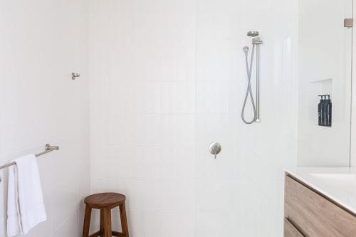 a white bathroom with a shower and a wooden stool at The Elm Apartments - The Yellow Room in Orange